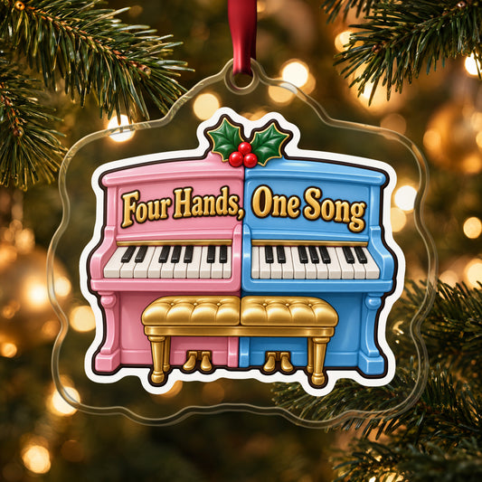 Four Hands, One Song Piano Duet clear acrylic Christmas ornament hanging on a lit Christmas tree with warm gold lights