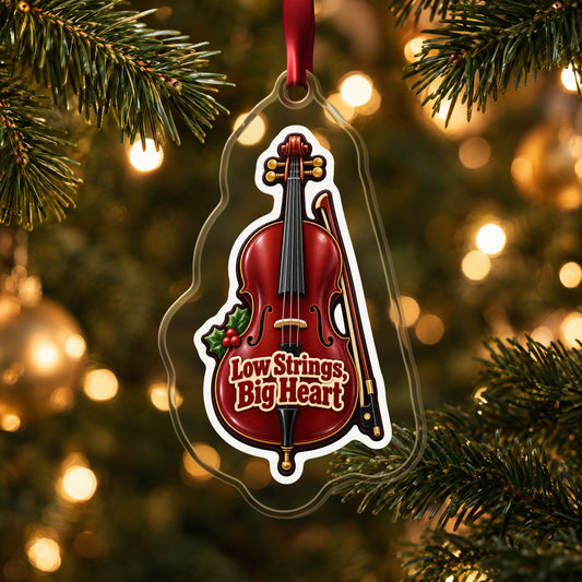 Low Strings, Big Heart Cello clear acrylic Christmas ornament hanging on a lit Christmas tree with warm gold lights