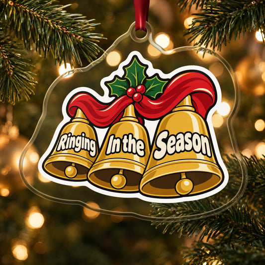 Ringing In the Season Handbells clear acrylic Christmas ornament hanging on a lit Christmas tree with warm gold lights