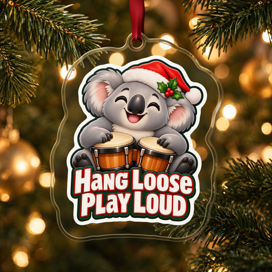 Hang Loose, Play Loud Koala Bongo clear acrylic Christmas ornament hanging on a lit Christmas tree with warm gold lights