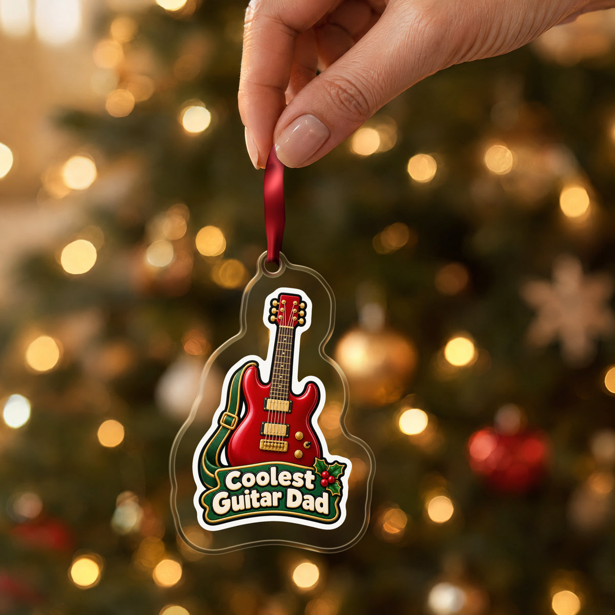 Coolest Guitar Dad clear acrylic Christmas ornament held by its red ribbon in a hand, shown at its real size