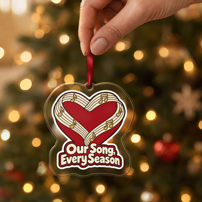 Our Song, Every Season Sheet Music Heart clear acrylic Christmas ornament held by its red ribbon in a hand, shown at its real size