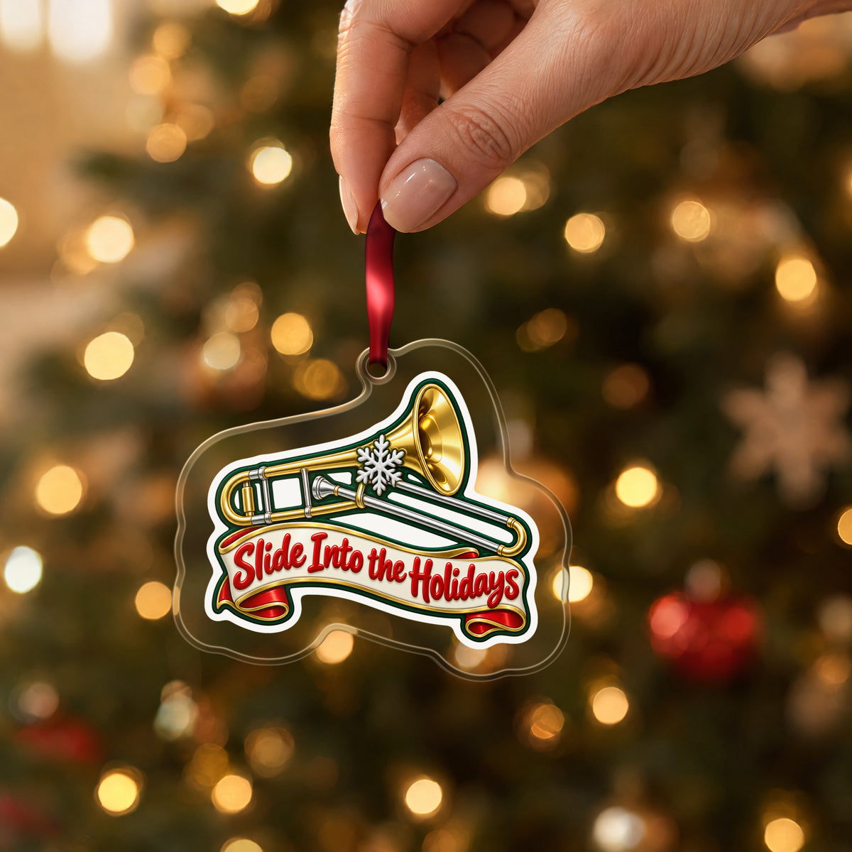 Slide Into the Holidays Trombone clear acrylic Christmas ornament held by its red ribbon in a hand, shown at its real size