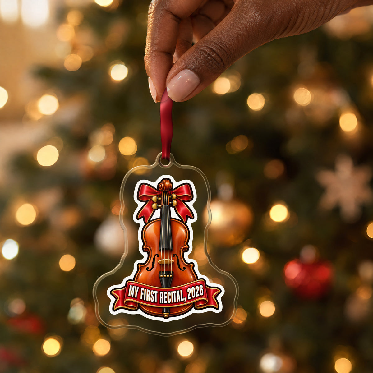 My First Violin Recital 2026 clear acrylic Christmas ornament held by its red ribbon in a hand, shown at its real size