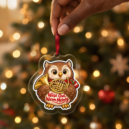 Wise Owl, Warm Melody French Horn clear acrylic Christmas ornament held by its red ribbon in a hand, shown at its real size