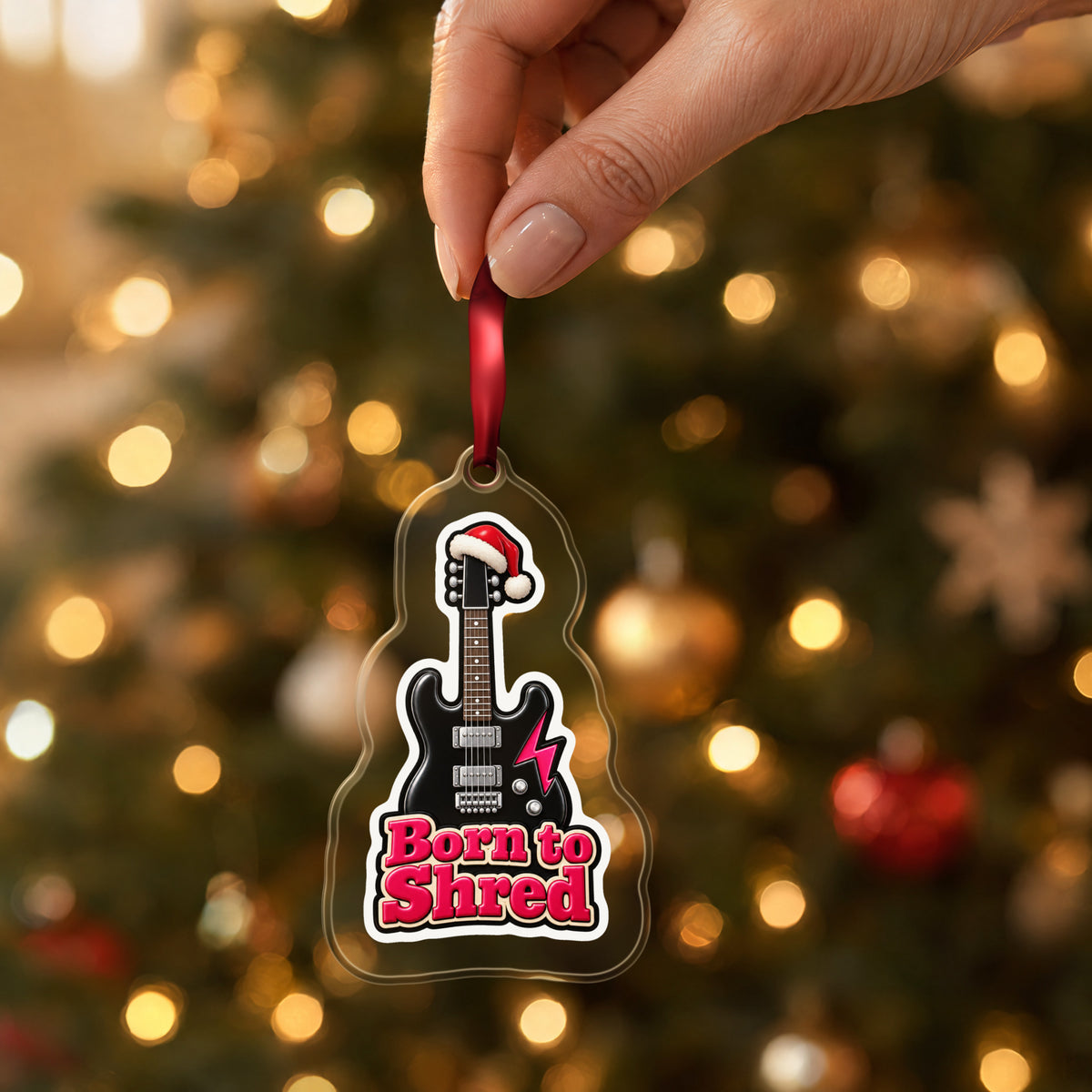 Born to Shred Electric Guitar clear acrylic Christmas ornament held by its red ribbon in a hand, shown at its real size