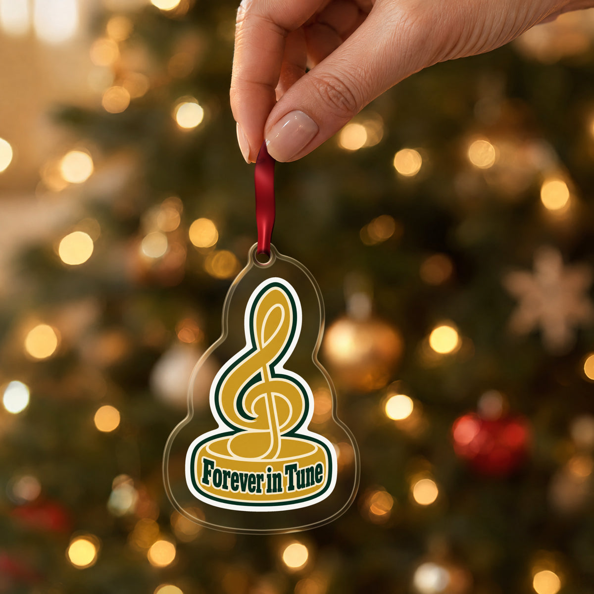 Forever in Tune Treble Clef clear acrylic Christmas ornament held by its red ribbon in a hand, shown at its real size