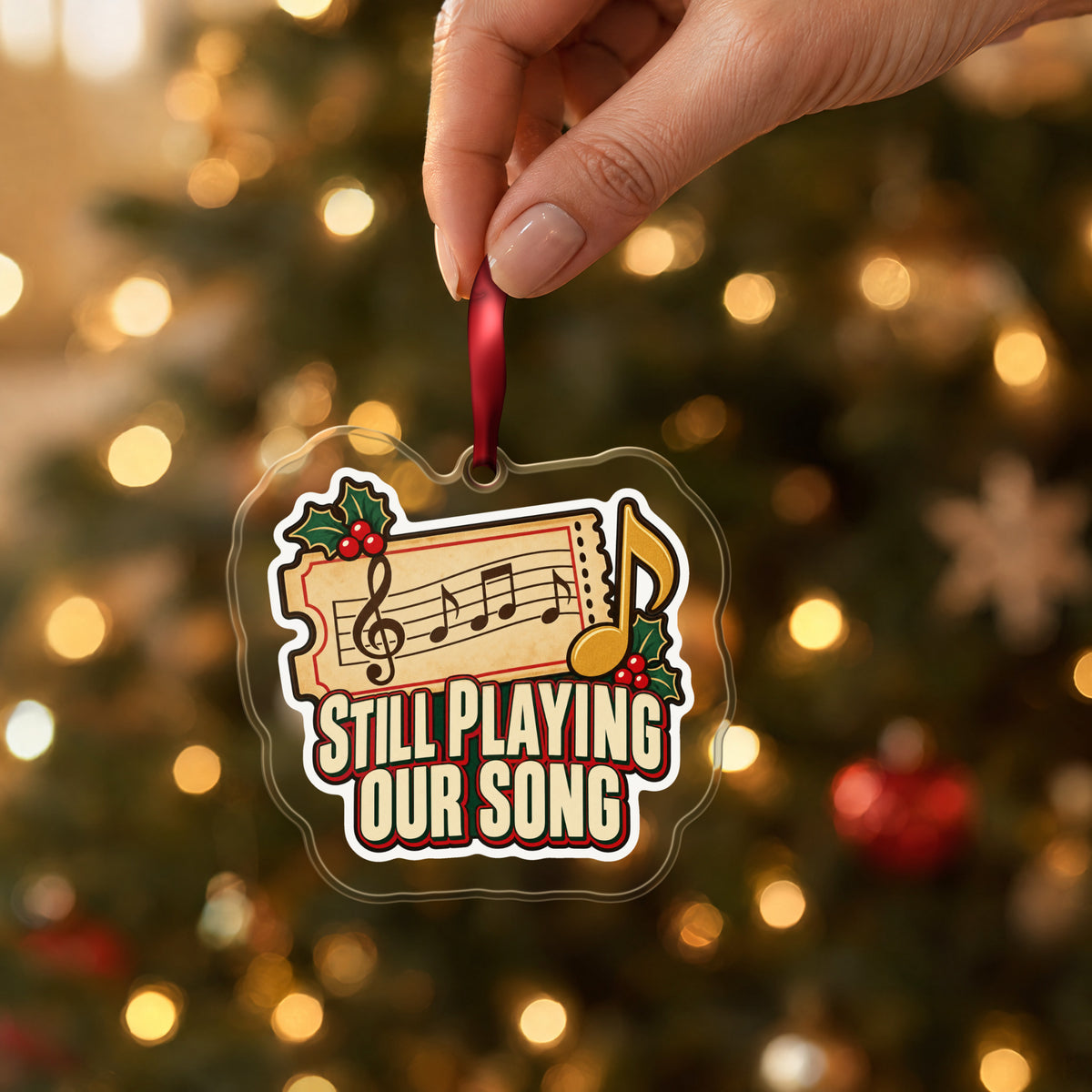 Still Playing Our Song Concert Ticket clear acrylic Christmas ornament held by its red ribbon in a hand, shown at its real size