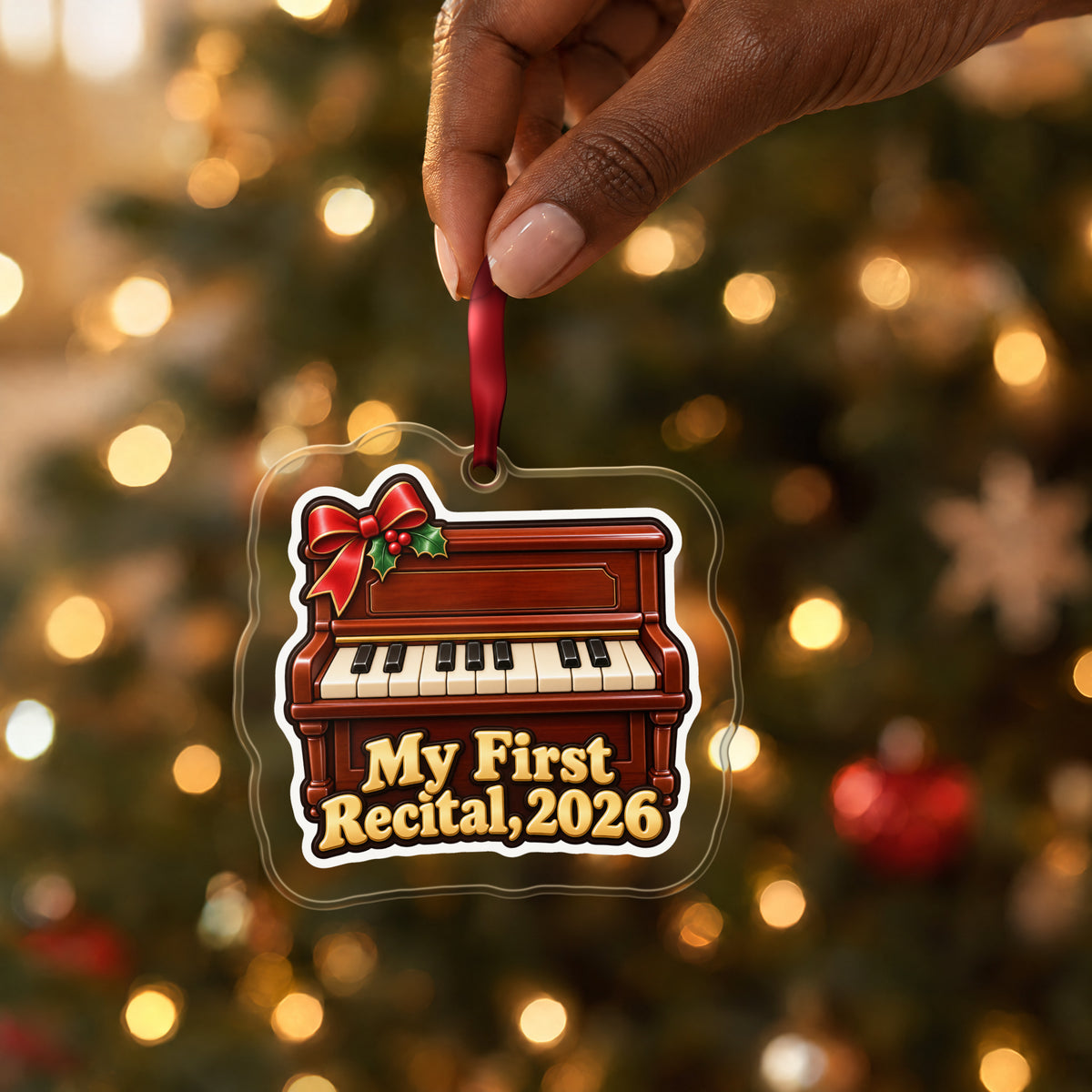 My First Piano Recital 2026 clear acrylic Christmas ornament held by its red ribbon in a hand, shown at its real size