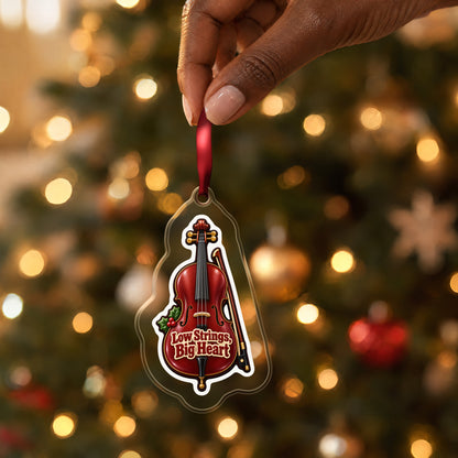 Low Strings, Big Heart Cello clear acrylic Christmas ornament held by its red ribbon in a hand, shown at its real size