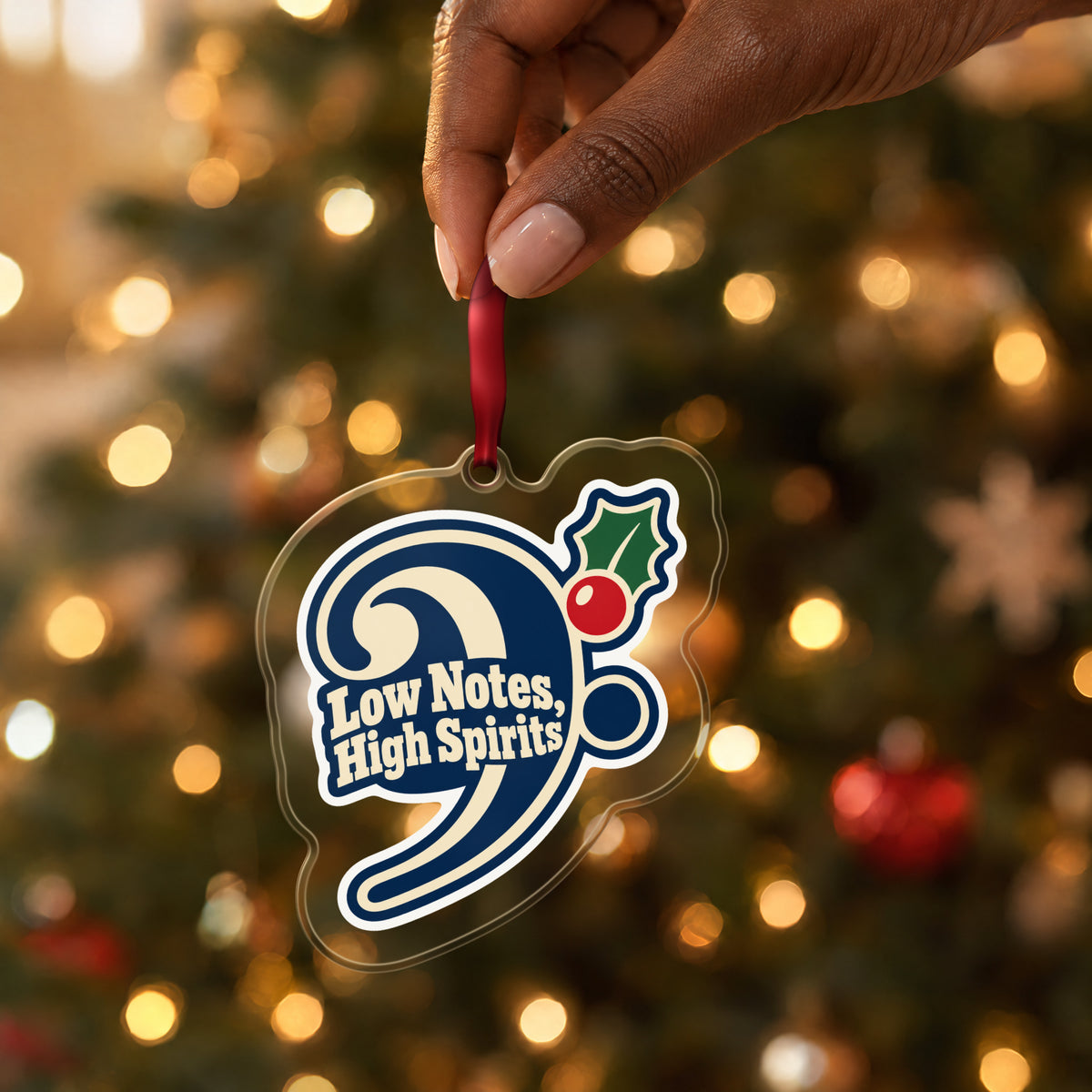 Low Notes, High Spirits Bass Clef clear acrylic Christmas ornament held by its red ribbon in a hand, shown at its real size