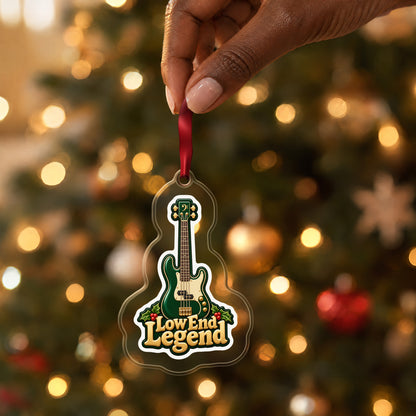 Low End Legend Bass Guitar clear acrylic Christmas ornament held by its red ribbon in a hand, shown at its real size