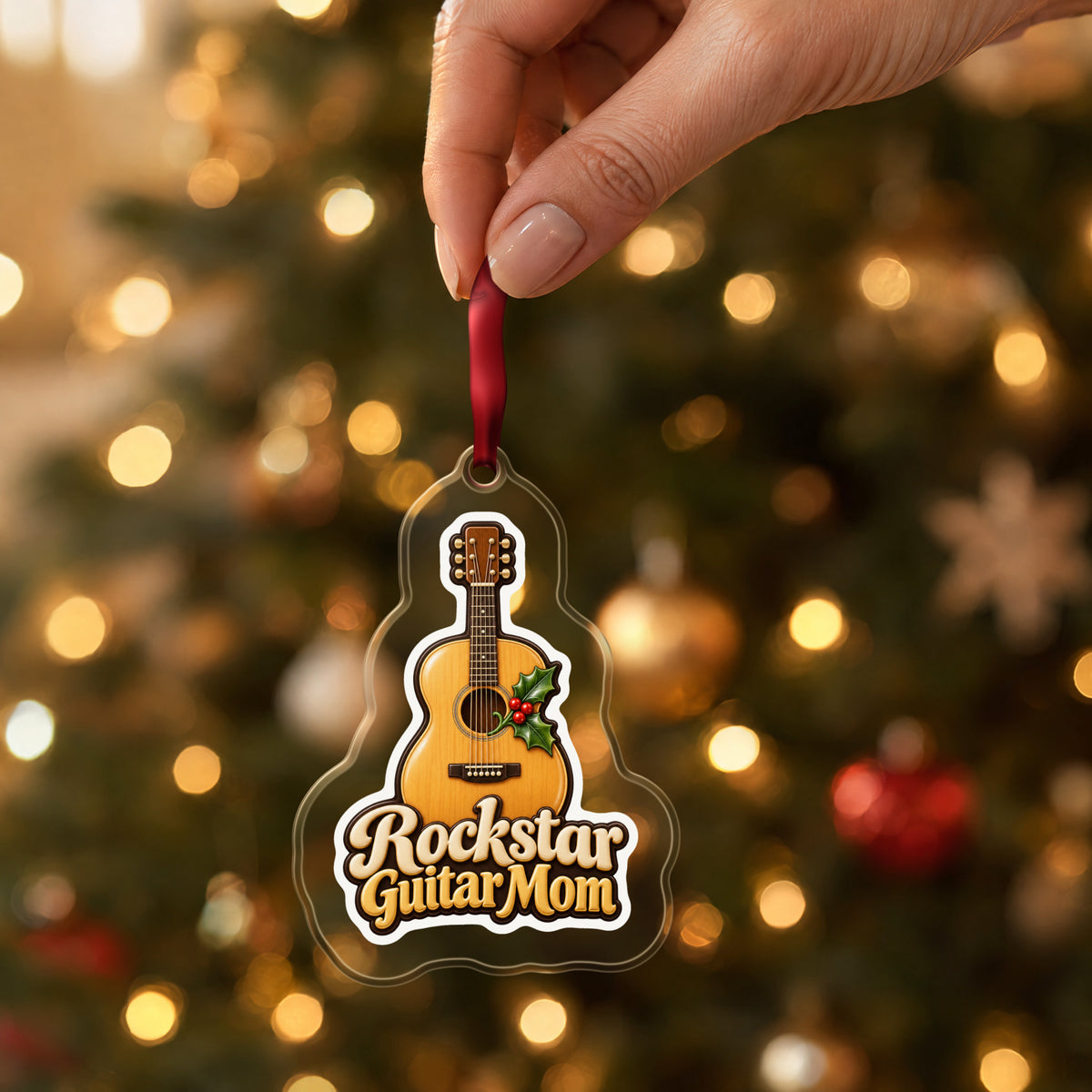 Rockstar Guitar Mom clear acrylic Christmas ornament held by its red ribbon in a hand, shown at its real size