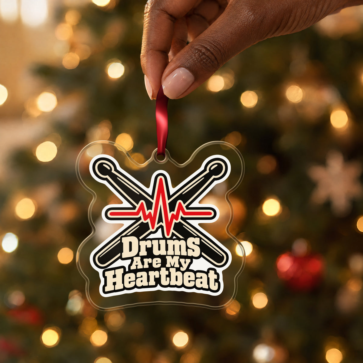 Drums Are My Heartbeat Drumsticks clear acrylic Christmas ornament held by its red ribbon in a hand, shown at its real size