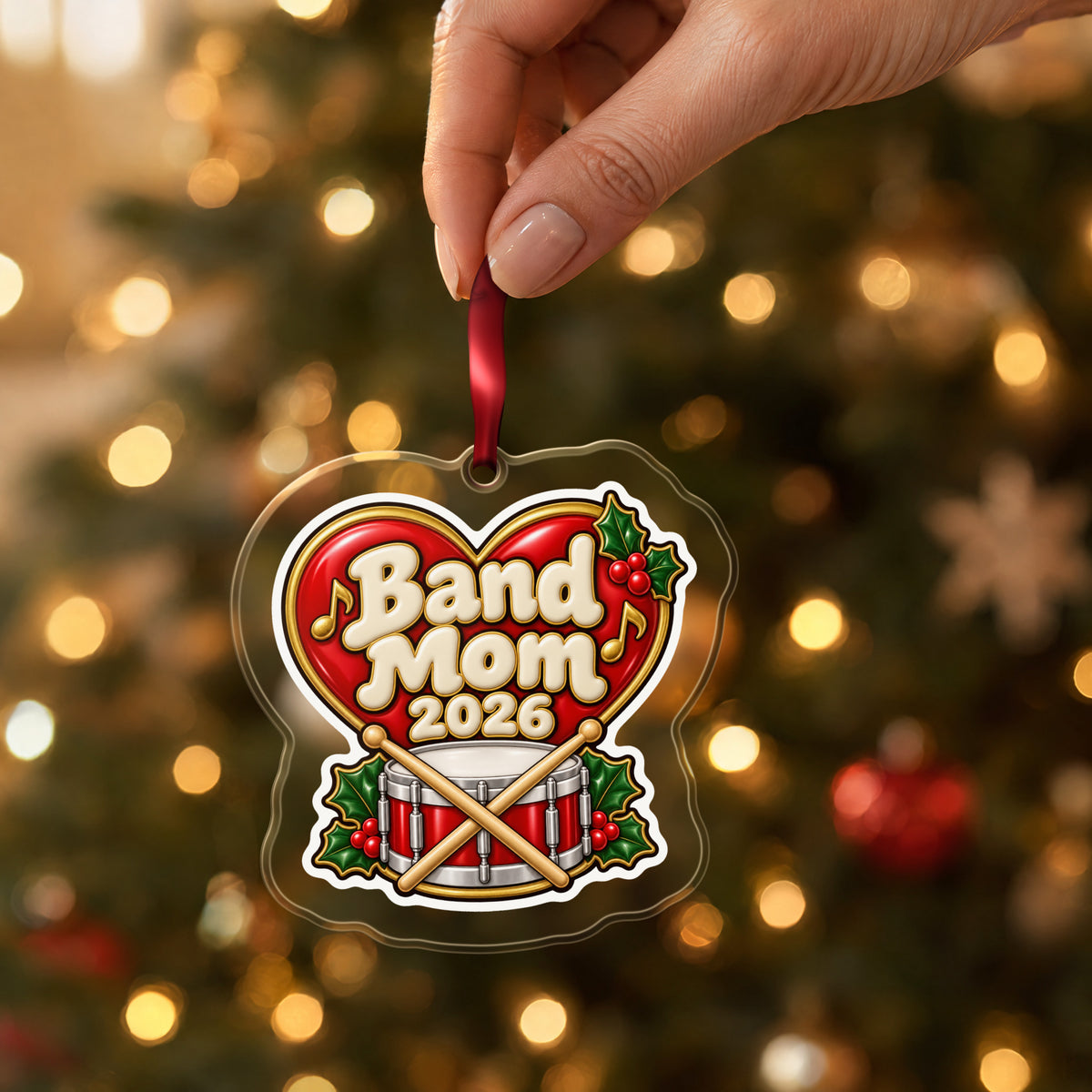 Band Mom 2026 clear acrylic Christmas ornament held by its red ribbon in a hand, shown at its real size