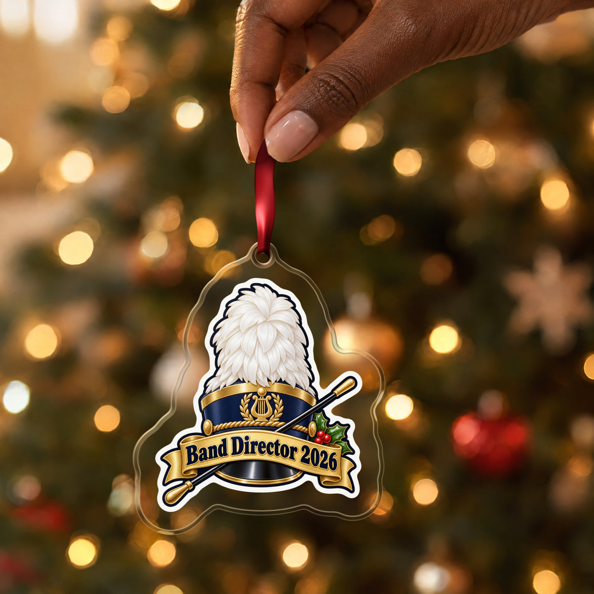Band Director 2026 clear acrylic Christmas ornament held by its red ribbon in a hand, shown at its real size