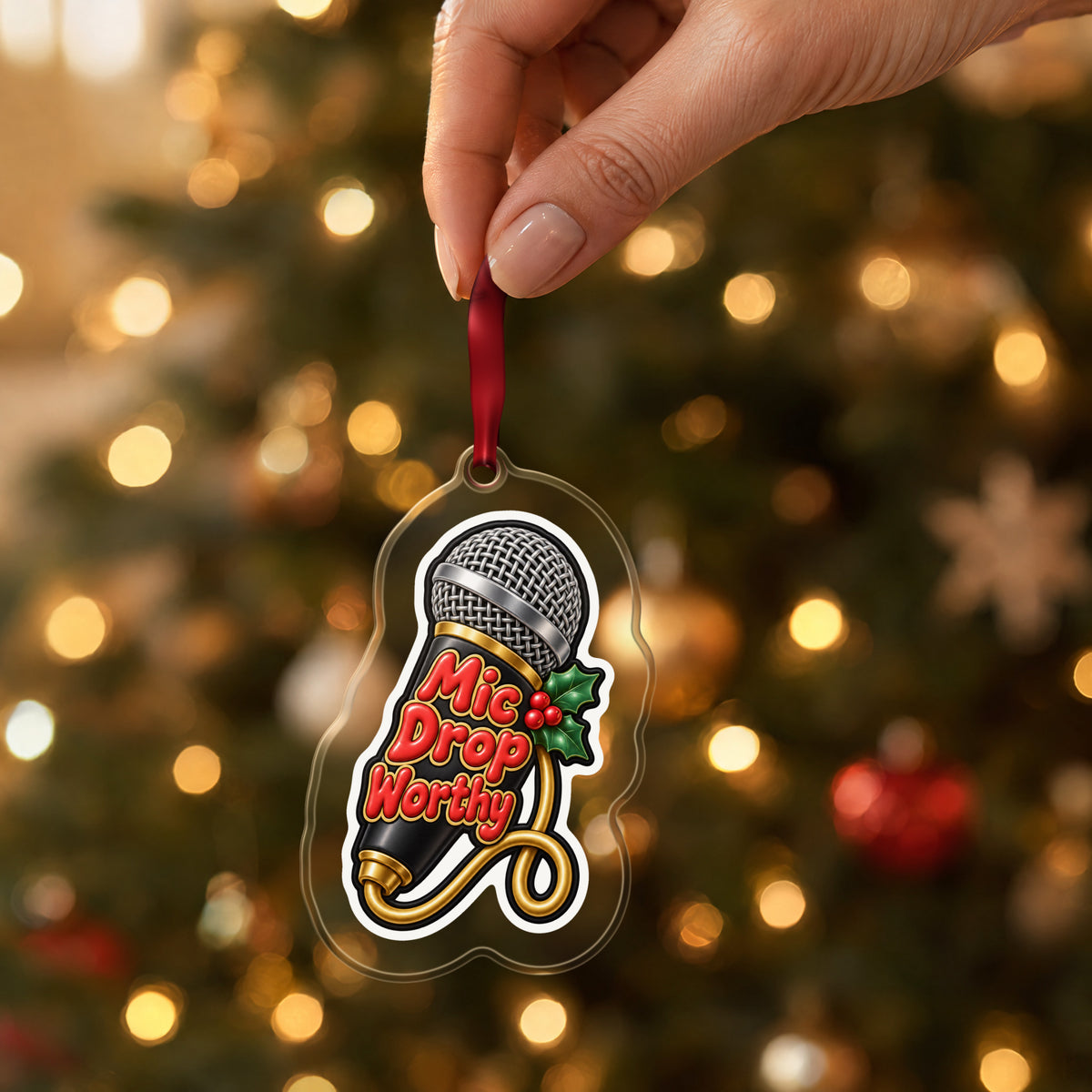 Mic Drop Worthy Microphone clear acrylic Christmas ornament held by its red ribbon in a hand, shown at its real size