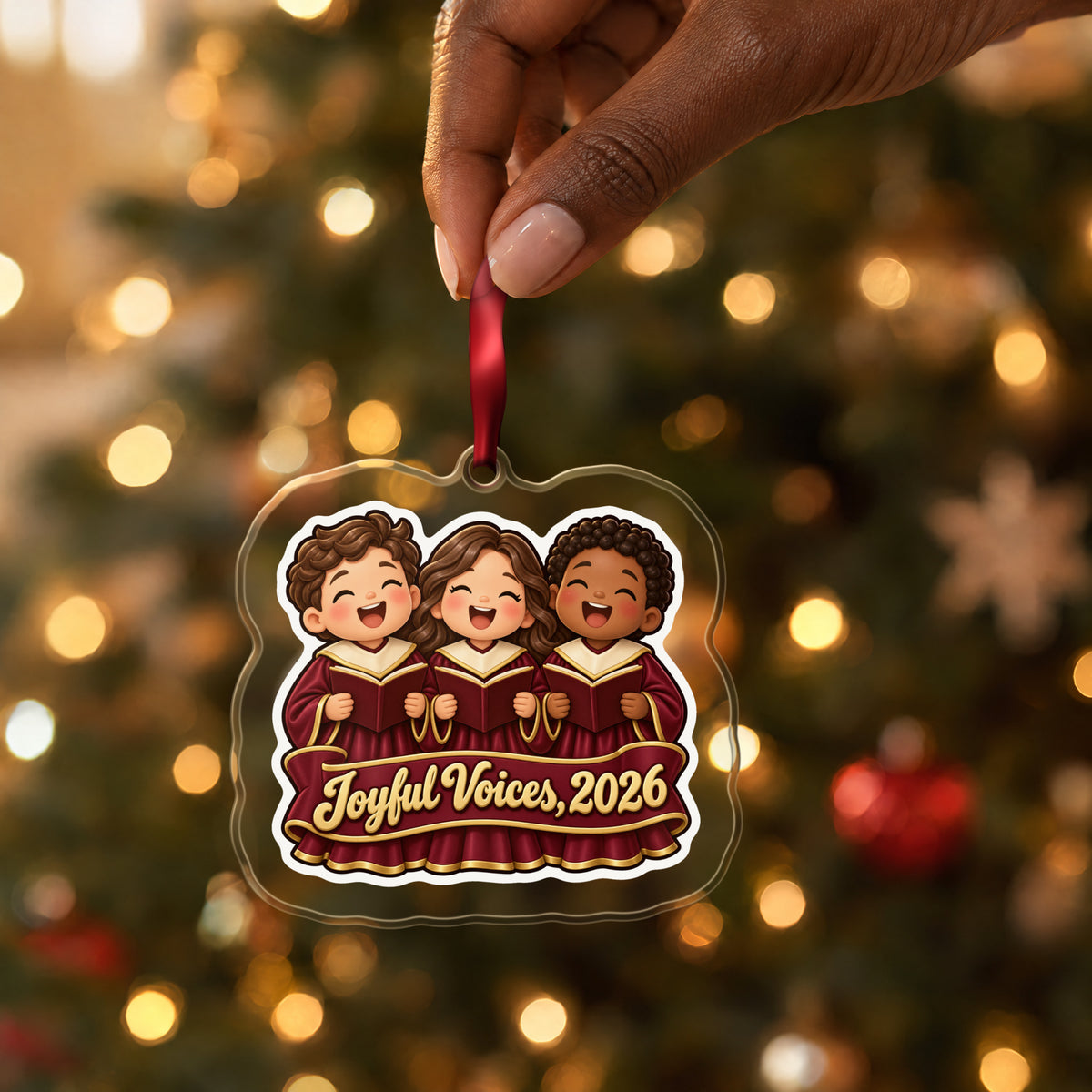 Joyful Voices 2026 Choir clear acrylic Christmas ornament held by its red ribbon in a hand, shown at its real size