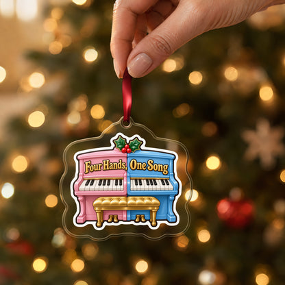 Four Hands, One Song Piano Duet clear acrylic Christmas ornament held by its red ribbon in a hand, shown at its real size