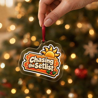 Chasing the Setlist Festival Ticket clear acrylic Christmas ornament held by its red ribbon in a hand, shown at its real size