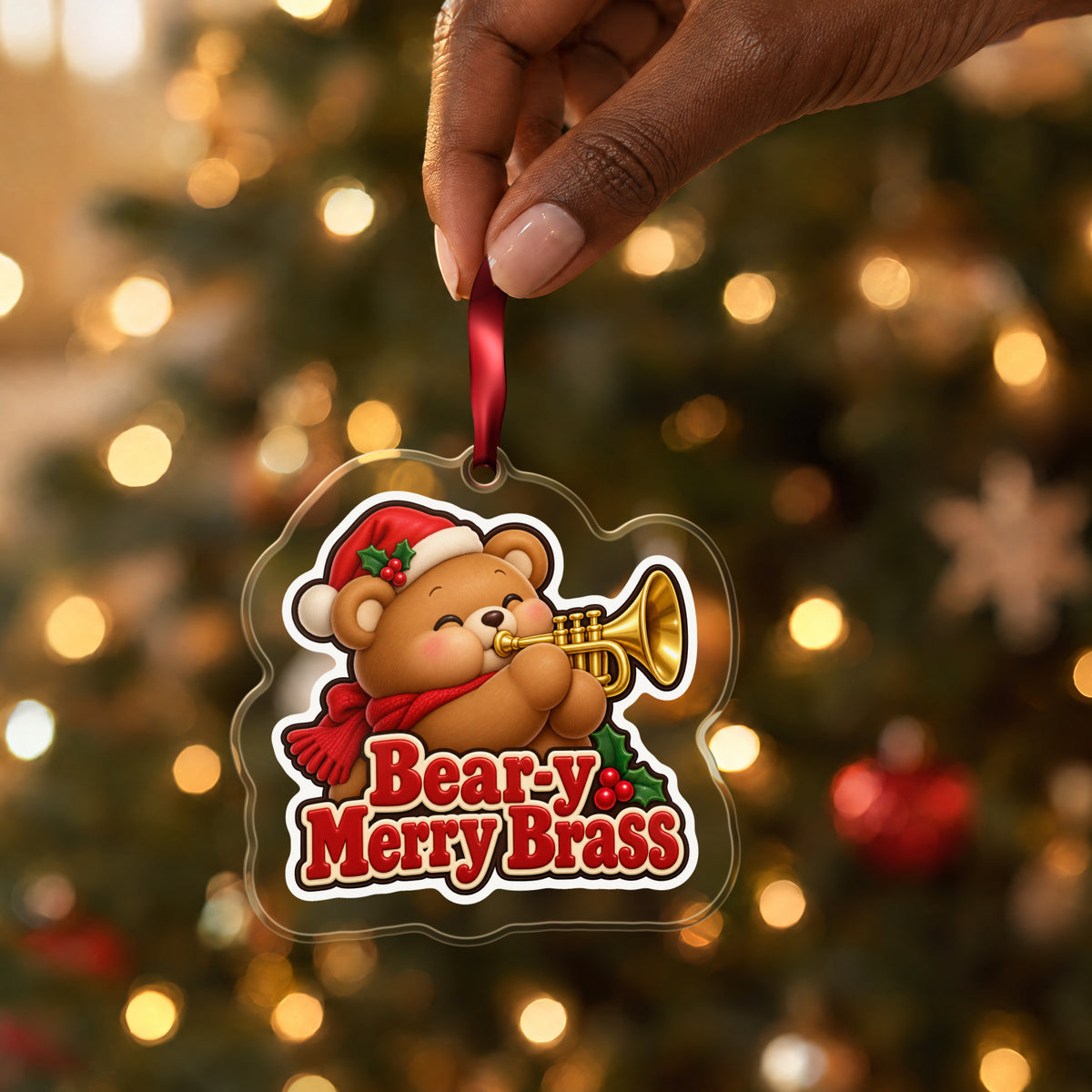 Bear-y Merry Brass Teddy Bear Trumpet clear acrylic Christmas ornament held by its red ribbon in a hand, shown at its real size