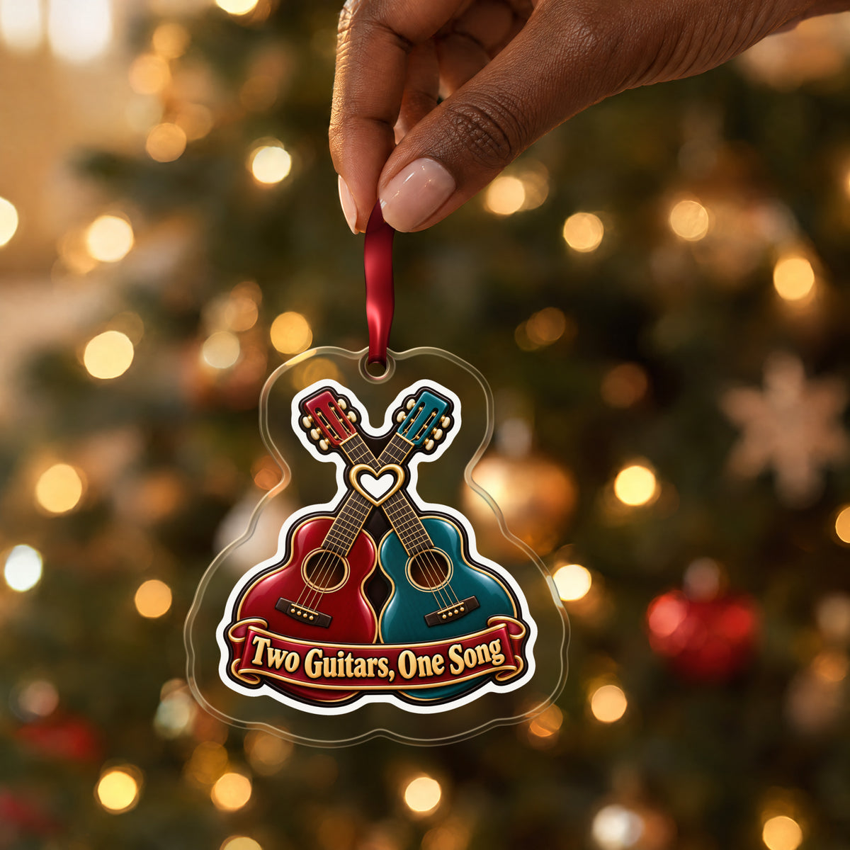 Two Guitars, One Song Couples clear acrylic Christmas ornament held by its red ribbon in a hand, shown at its real size