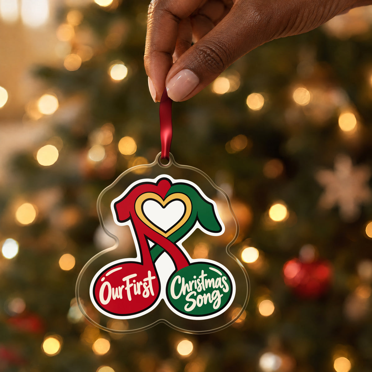 Our First Christmas Song Music Notes clear acrylic Christmas ornament held by its red ribbon in a hand, shown at its real size