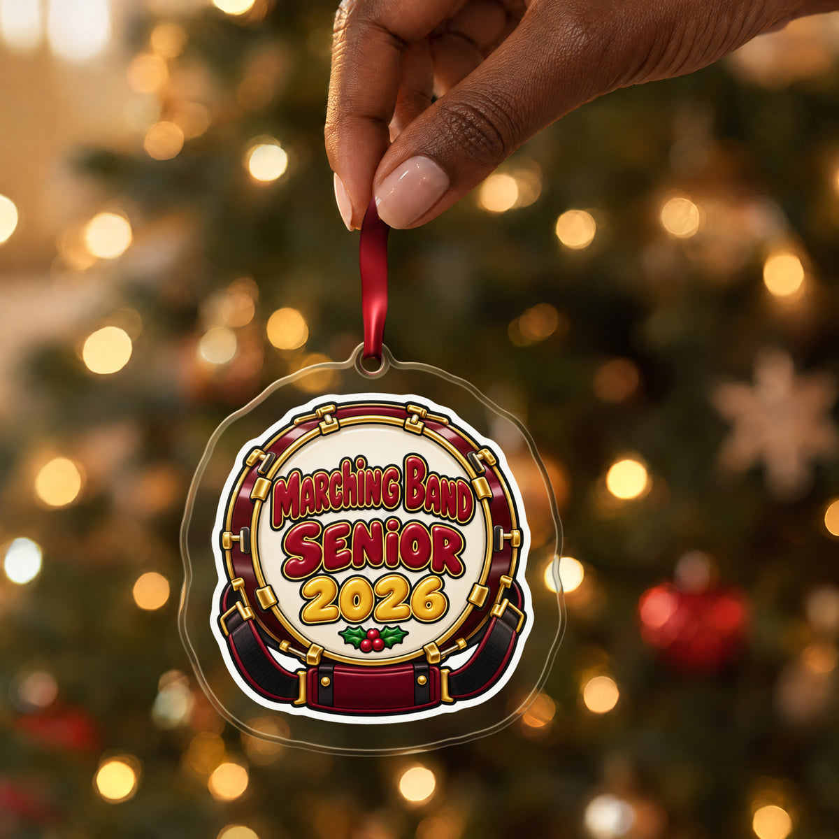 Marching Band Senior 2026 clear acrylic Christmas ornament held by its red ribbon in a hand, shown at its real size