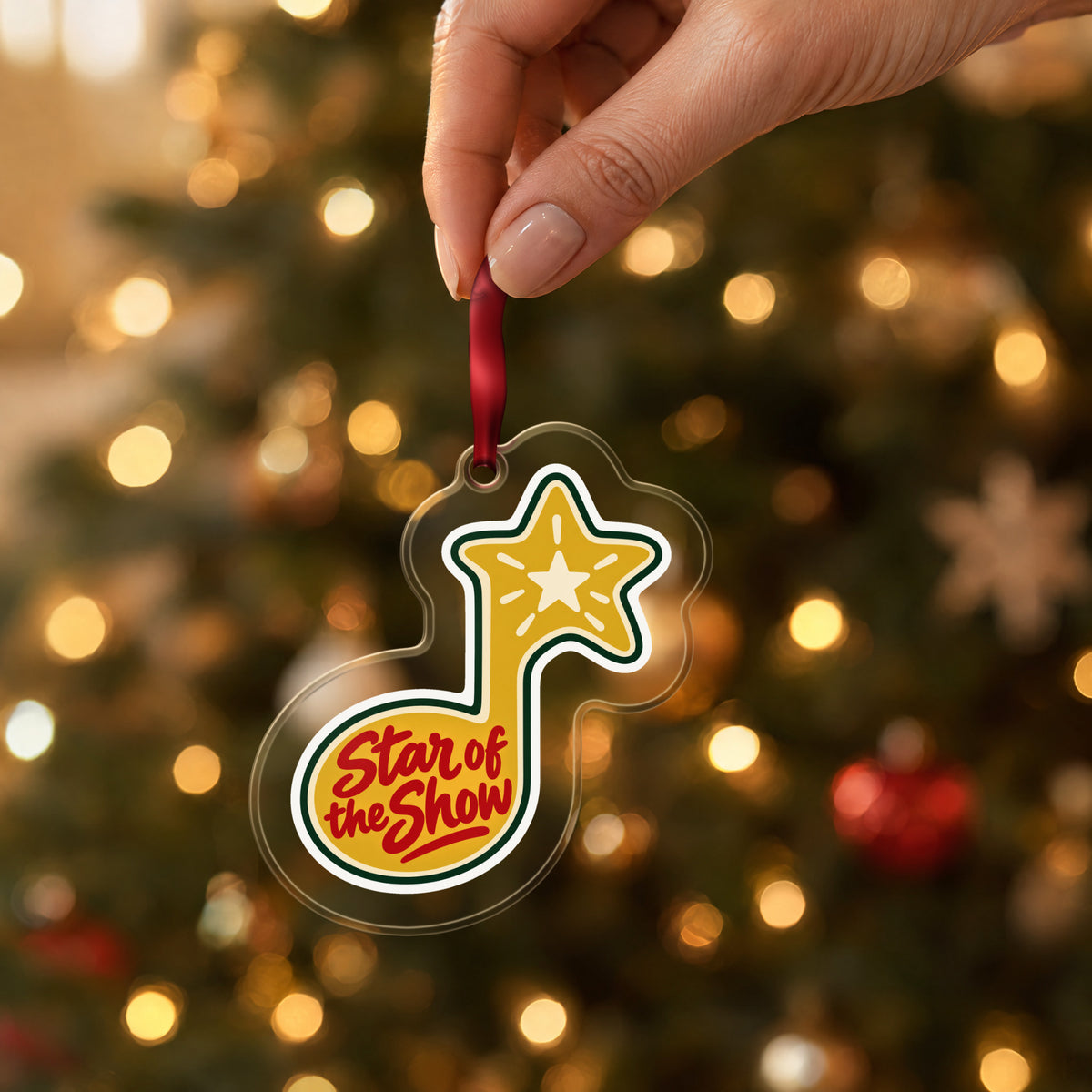 Star of the Show Music Note clear acrylic Christmas ornament held by its red ribbon in a hand, shown at its real size