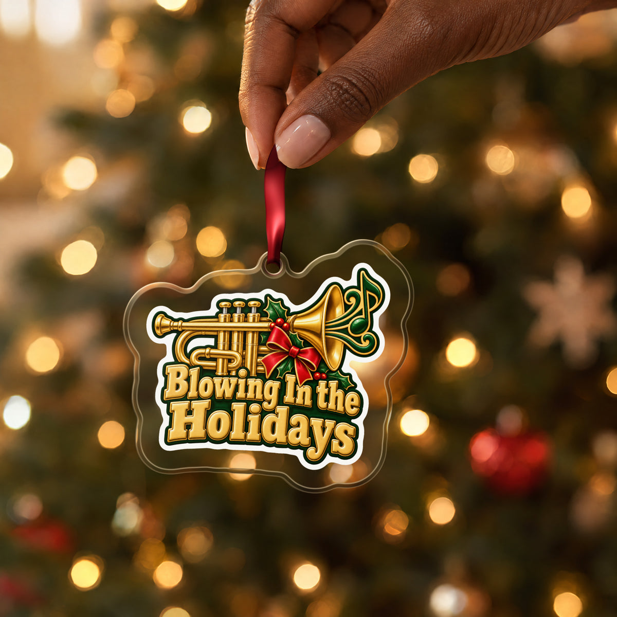 Blowing In the Holidays Trumpet clear acrylic Christmas ornament held by its red ribbon in a hand, shown at its real size