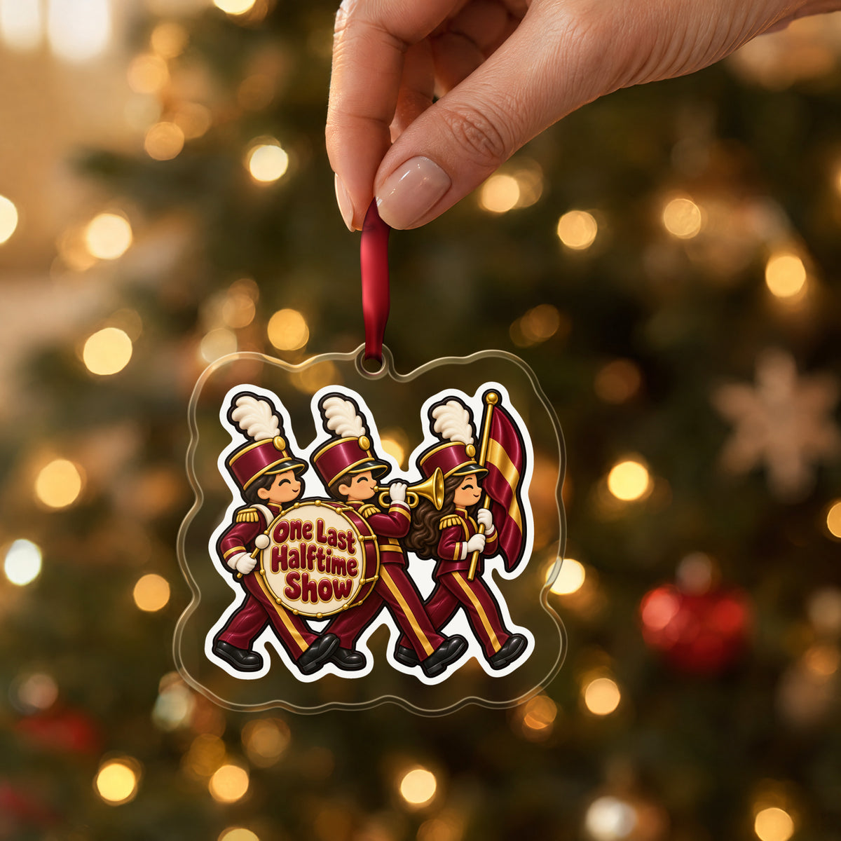 One Last Halftime Show Marching Band clear acrylic Christmas ornament held by its red ribbon in a hand, shown at its real size