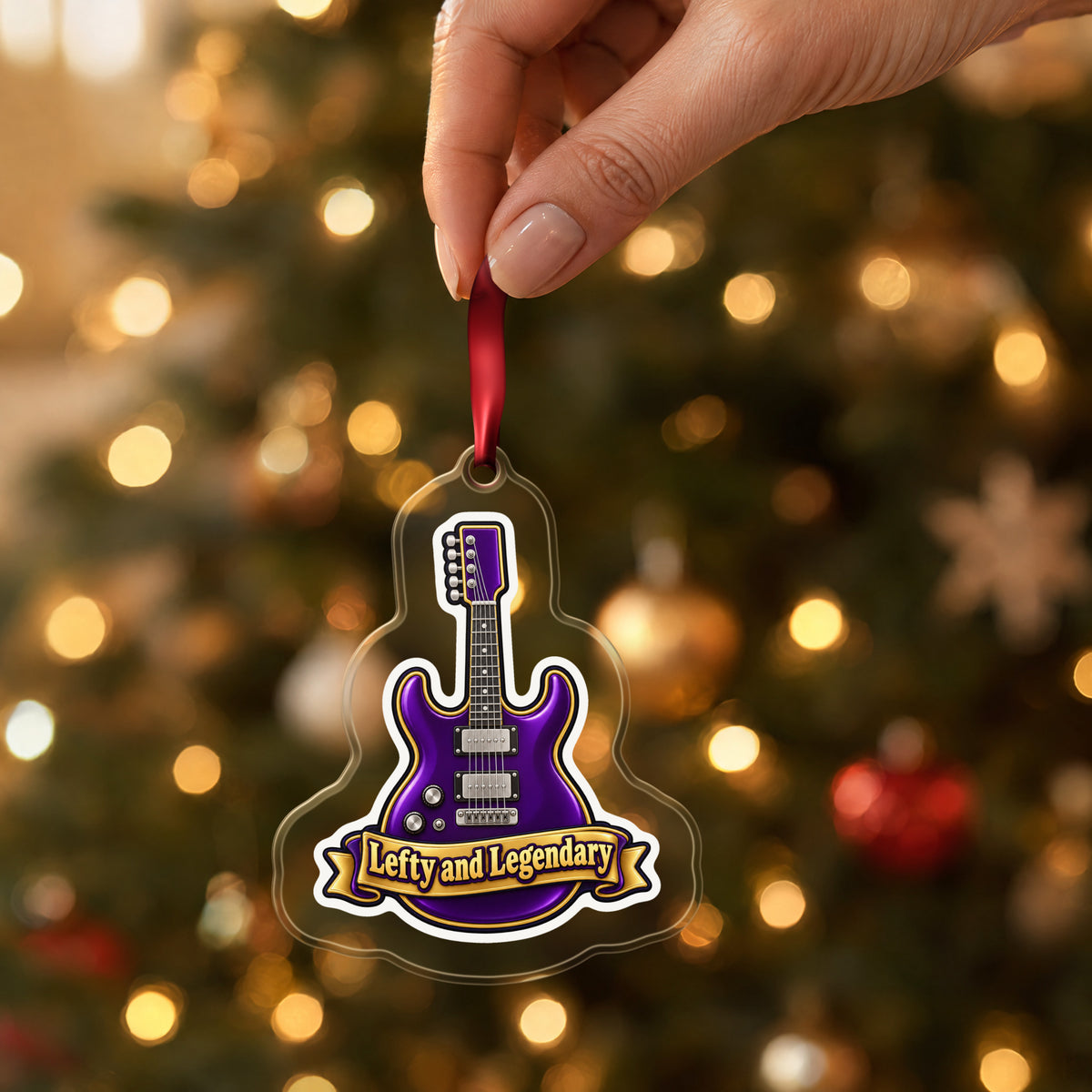 Lefty and Legendary Electric Guitar clear acrylic Christmas ornament held by its red ribbon in a hand, shown at its real size