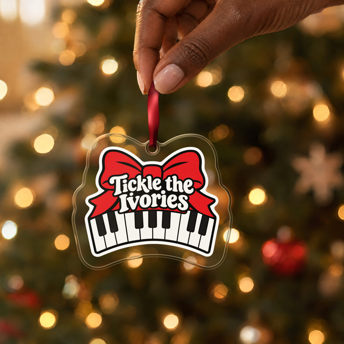 Tickle the Ivories Piano Keys clear acrylic Christmas ornament held by its red ribbon in a hand, shown at its real size