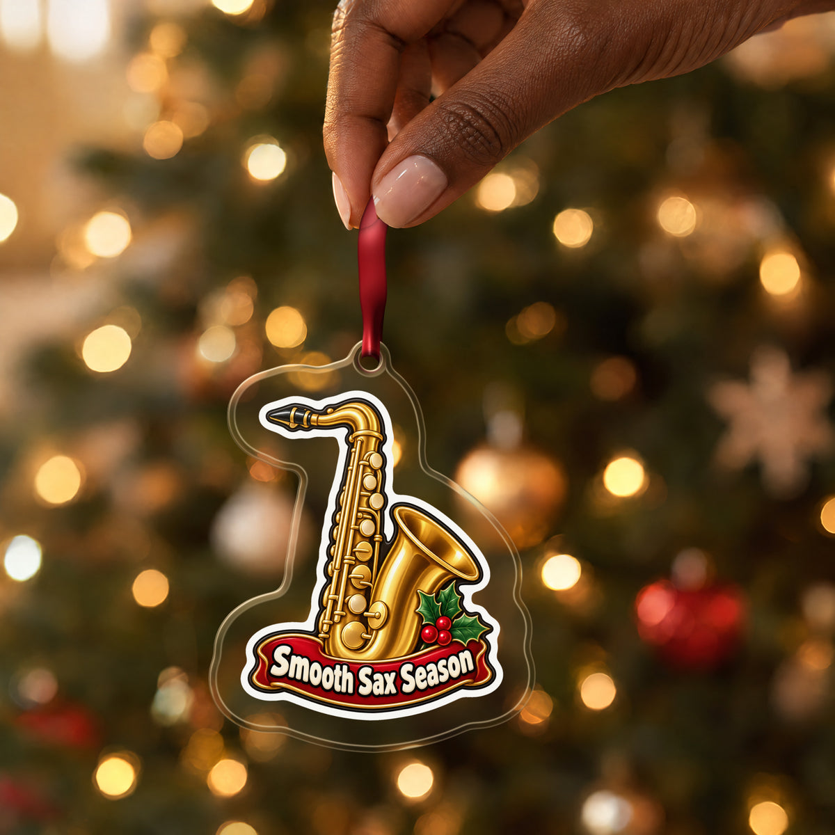 Smooth Sax Season Saxophone clear acrylic Christmas ornament held by its red ribbon in a hand, shown at its real size