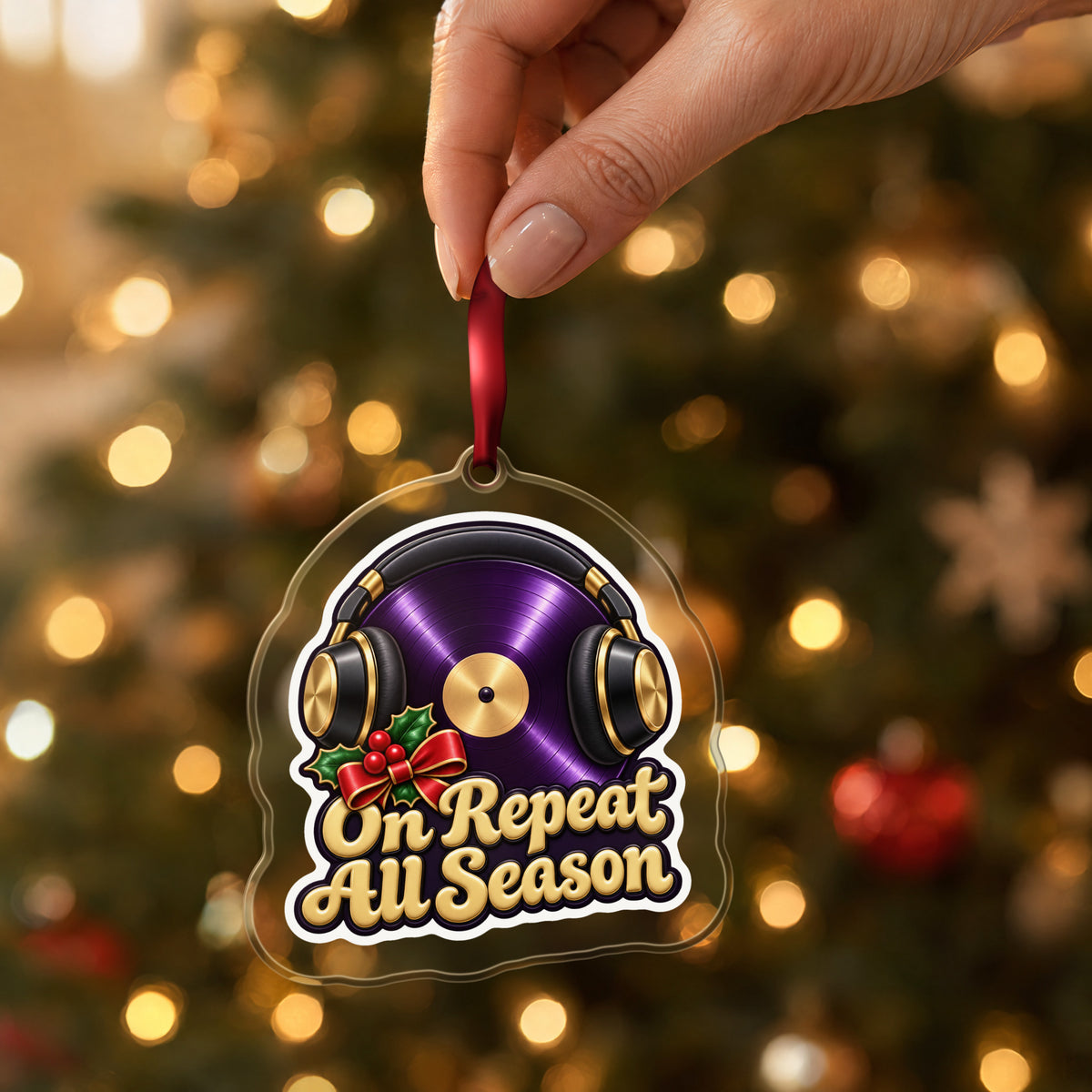On Repeat Vinyl and Headphones clear acrylic Christmas ornament held by its red ribbon in a hand, shown at its real size