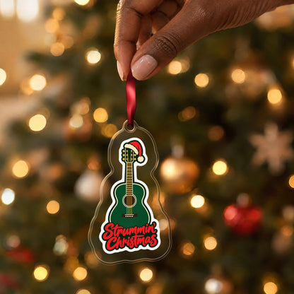 Strummin' Christmas Acoustic Guitar clear acrylic Christmas ornament held by its red ribbon in a hand, shown at its real size