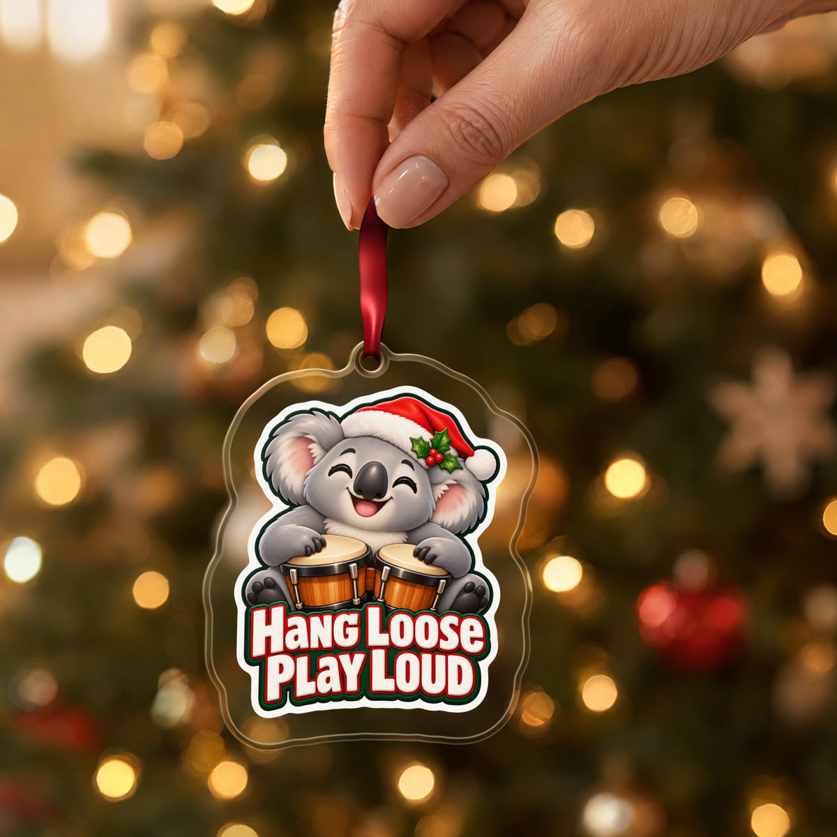 Hang Loose, Play Loud Koala Bongo clear acrylic Christmas ornament held by its red ribbon in a hand, shown at its real size