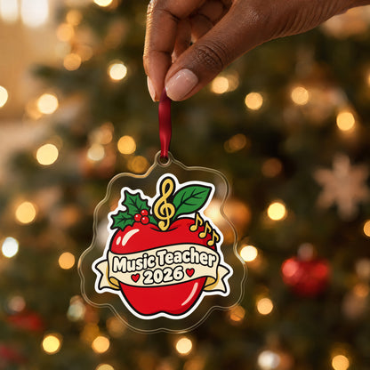 Music Teacher 2026 clear acrylic Christmas ornament held by its red ribbon in a hand, shown at its real size