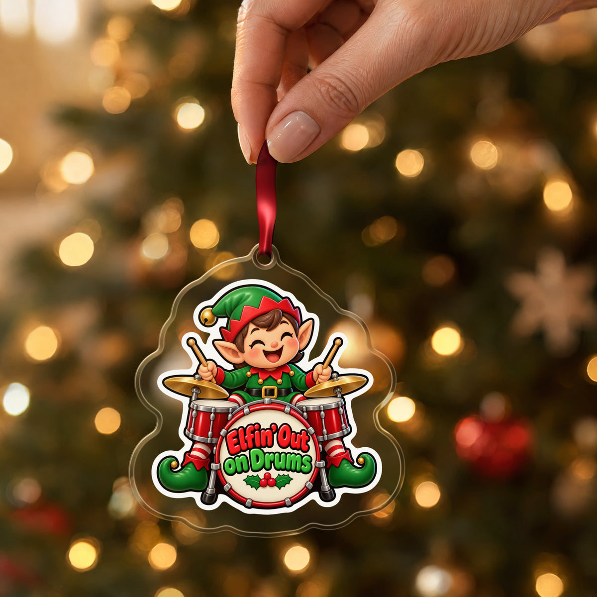 Elfin' Out on Drums Elf Drummer clear acrylic Christmas ornament held by its red ribbon in a hand, shown at its real size
