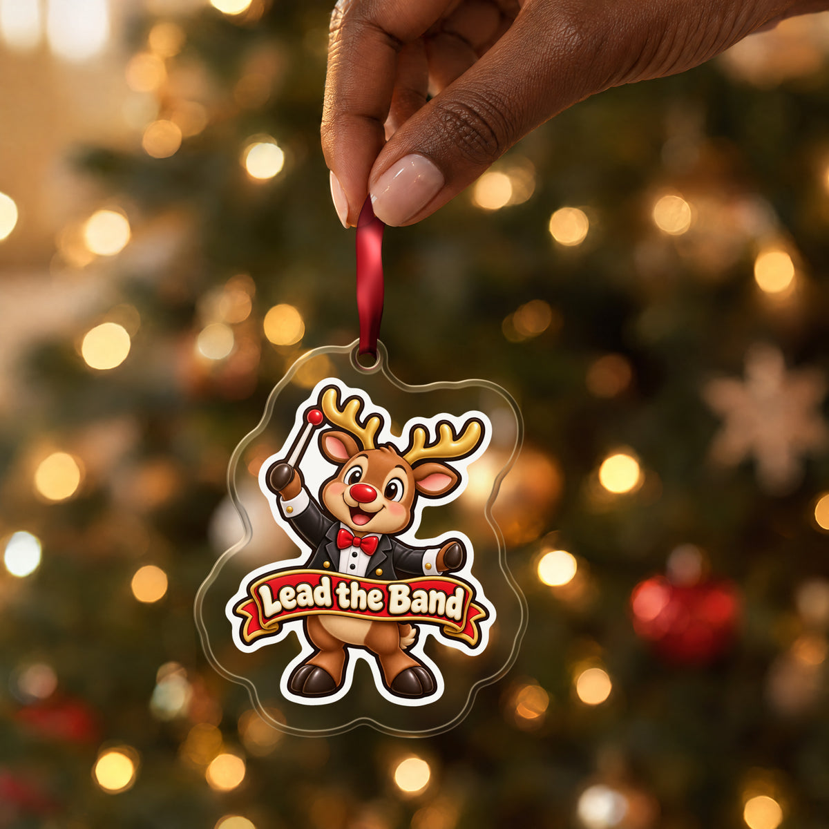Lead the Band Reindeer Conductor clear acrylic Christmas ornament held by its red ribbon in a hand, shown at its real size