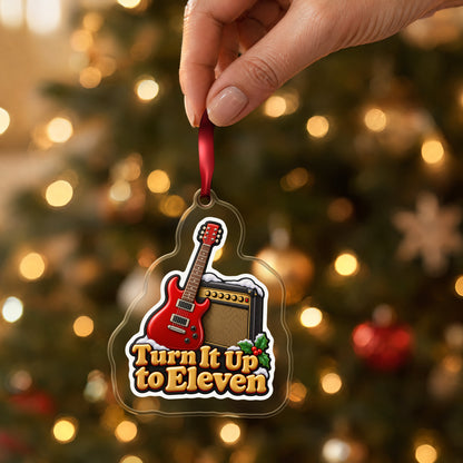 Turn It Up to Eleven Guitar and Amp clear acrylic Christmas ornament held by its red ribbon in a hand, shown at its real size