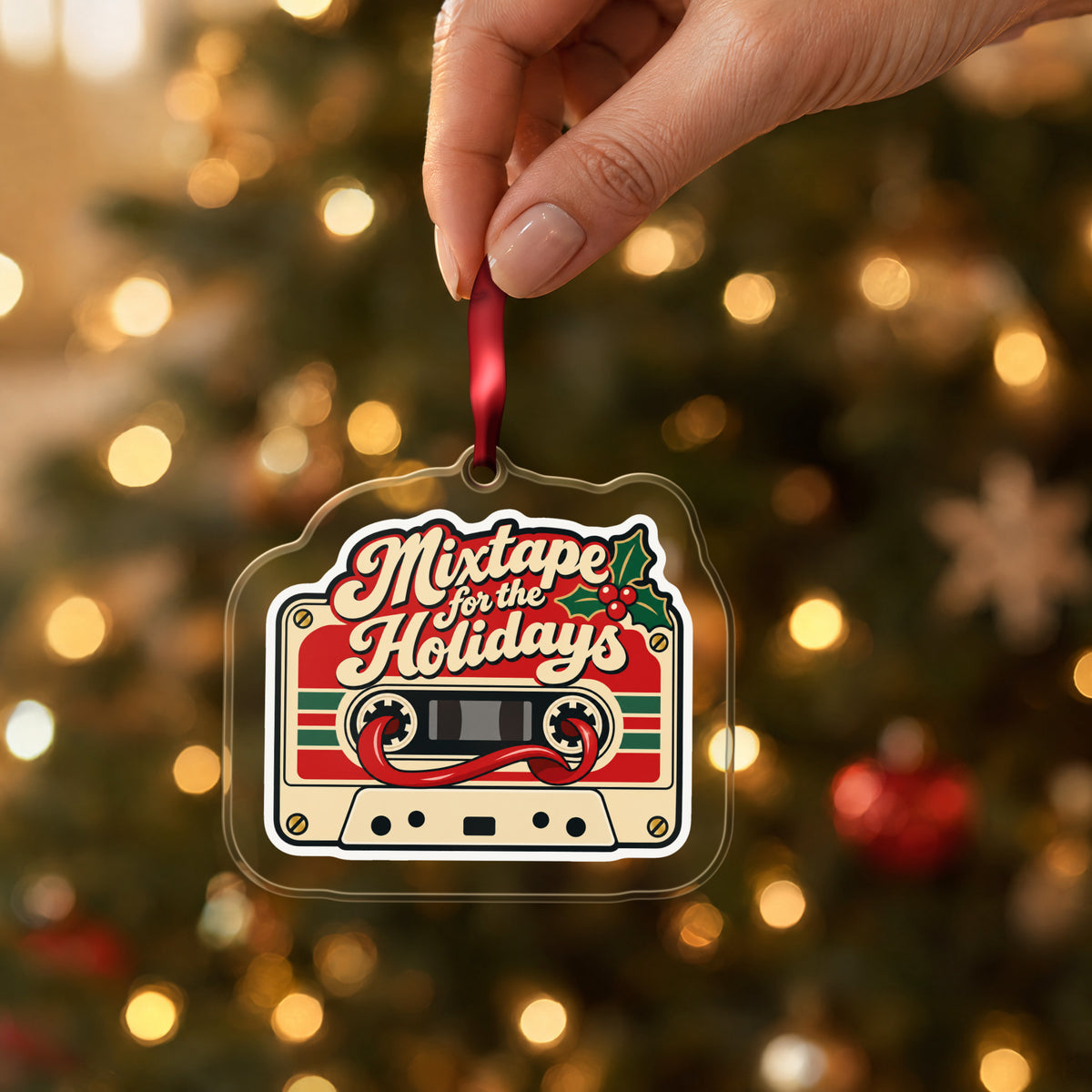 Mixtape for the Holidays Cassette clear acrylic Christmas ornament held by its red ribbon in a hand, shown at its real size