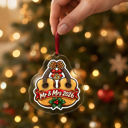 Mr & Mrs First Christmas 2026 Guitar clear acrylic Christmas ornament held by its red ribbon in a hand, shown at its real size
