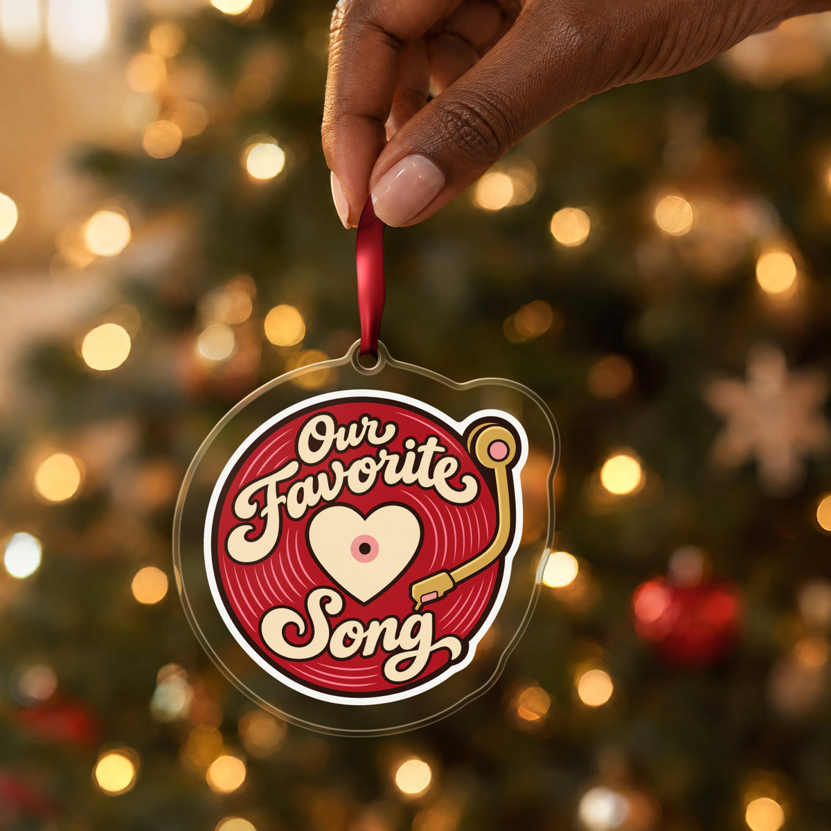 Our Favorite Song Vinyl Record clear acrylic Christmas ornament held by its red ribbon in a hand, shown at its real size