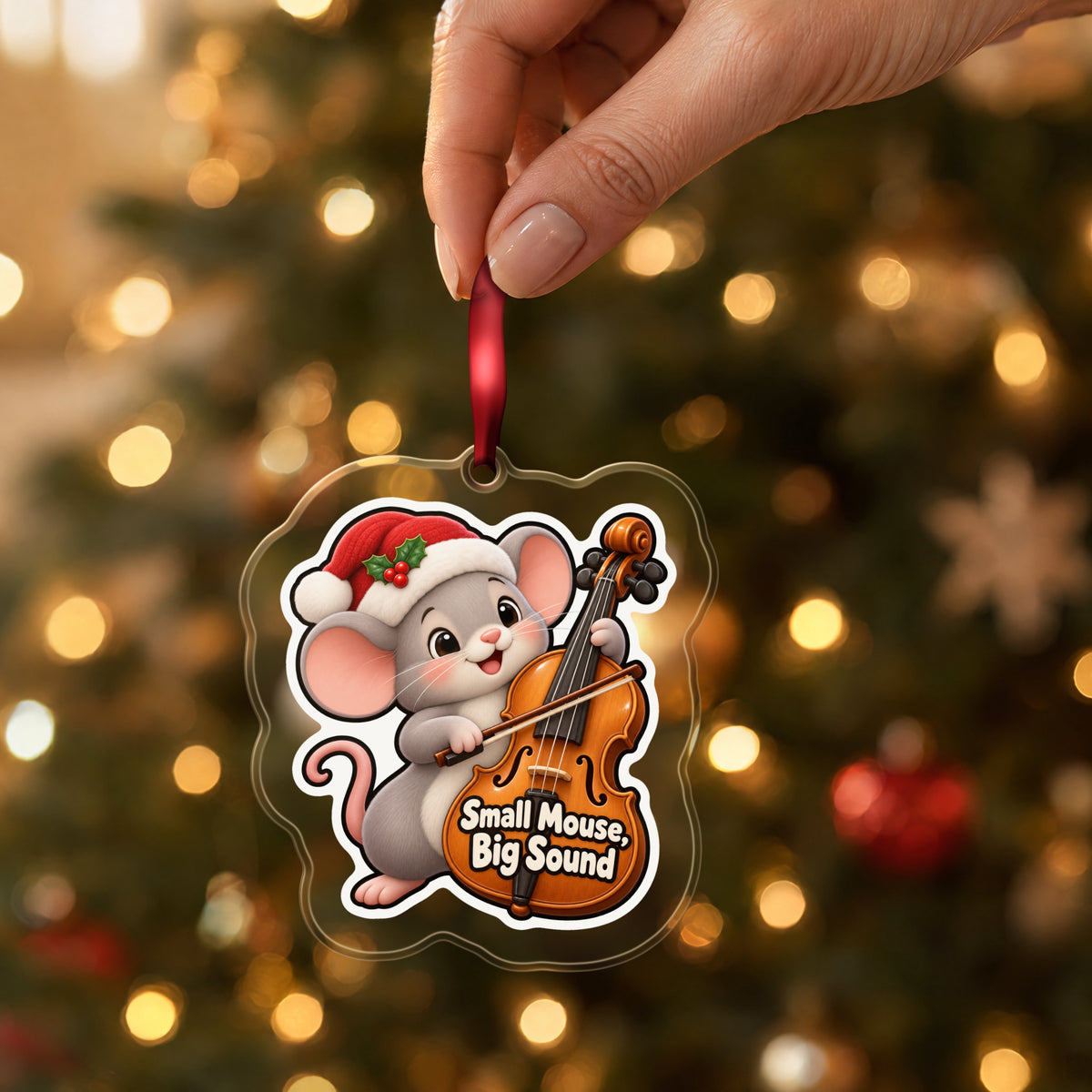 Small Mouse, Big Sound Cello clear acrylic Christmas ornament held by its red ribbon in a hand, shown at its real size