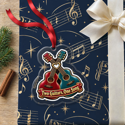 Two Guitars, One Song Couples clear acrylic Christmas ornament lying on a gift wrapped in Rhythm and Beat music wrapping paper