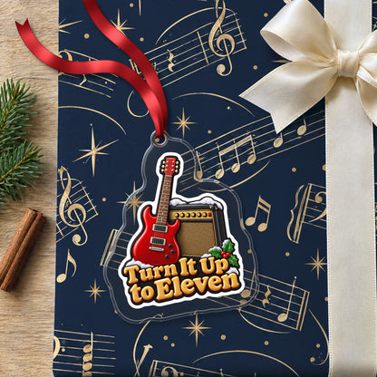 Turn It Up to Eleven Guitar and Amp clear acrylic Christmas ornament lying on a gift wrapped in Rhythm and Beat music wrapping paper