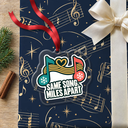 Same Song, Miles Apart Long Distance clear acrylic Christmas ornament lying on a gift wrapped in Rhythm and Beat music wrapping paper