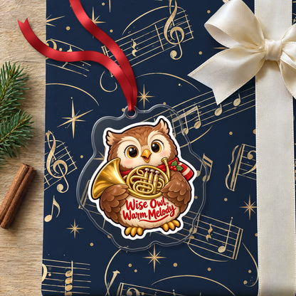 Wise Owl, Warm Melody French Horn clear acrylic Christmas ornament lying on a gift wrapped in Rhythm and Beat music wrapping paper