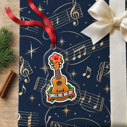 Small Uke, Big Joy Ukulele clear acrylic Christmas ornament lying on a gift wrapped in Rhythm and Beat music wrapping paper